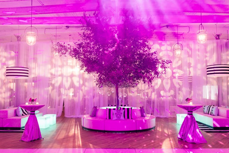 Purple lighted lounge area with fake tree and bar tables | PartySlate