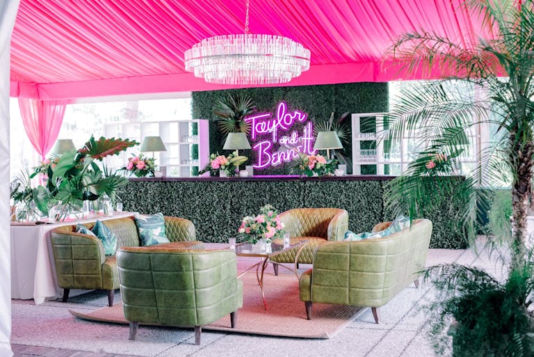 Pink tented bar area with olive green couches and plenty of greenery and pink neon sign | PartySlate