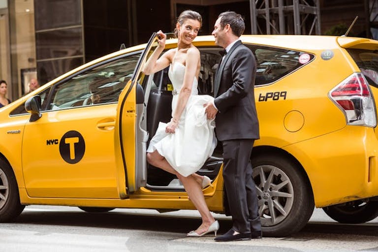 Bride escorts groom both dressed in wedding attire into New York City cab | PartySlate