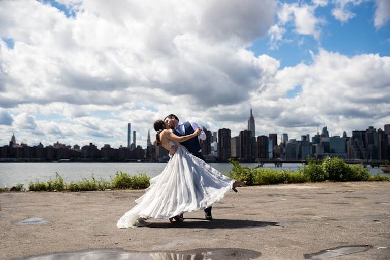 Bride and groom share a kiss on a sunny day backdropped by NYC skyline | PartySlate