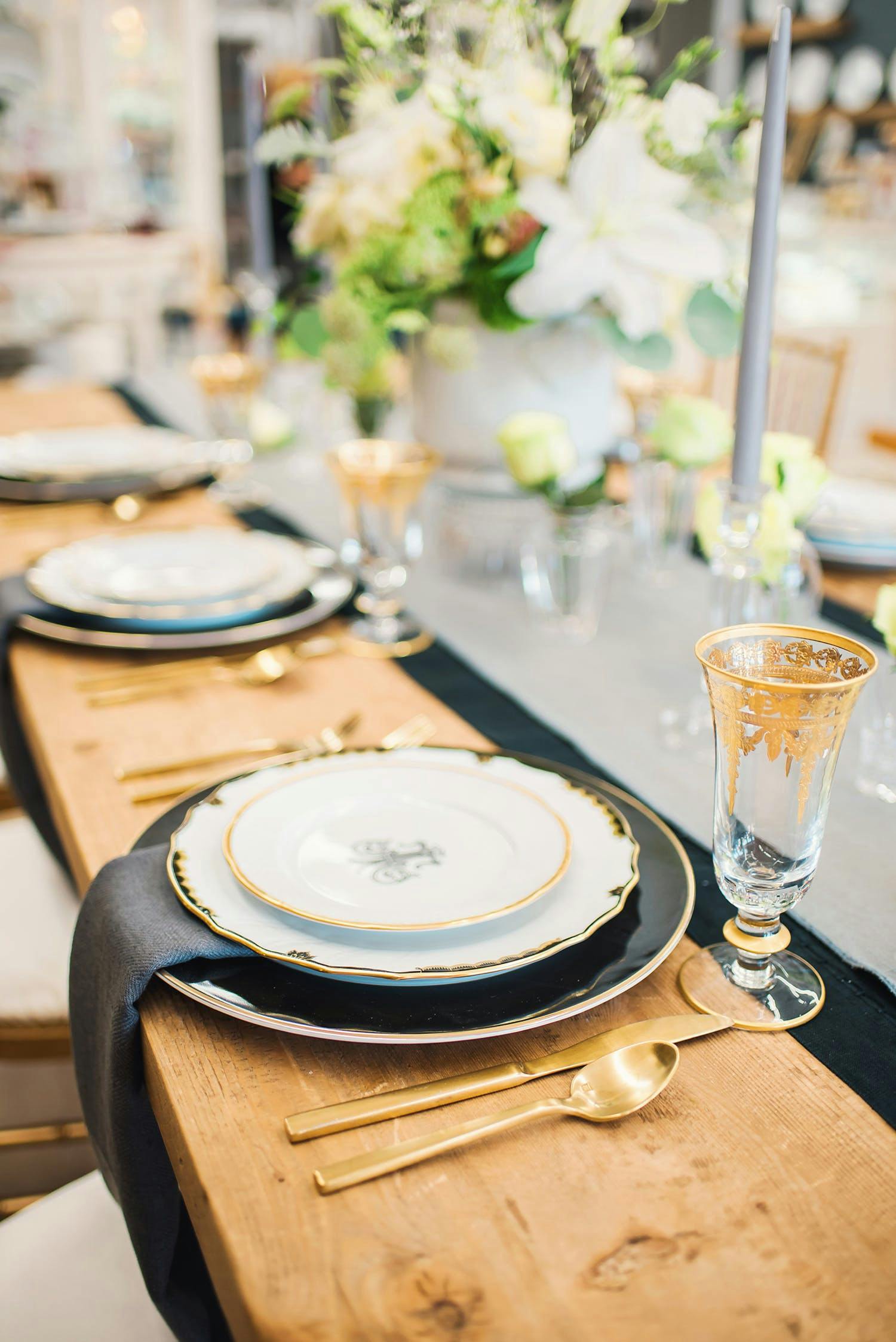 Fine dining table setting with gold cutlery and champagne glass atop wooden table | PartySlate