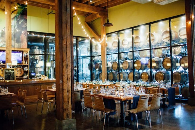 Dining area with by barrels behind paned glass and string lights at City Winery Chicago | PartySlate