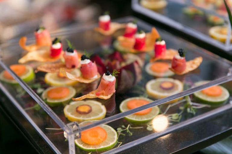 Delectable finger food atop innovative glass tray with decorative veggies beneath | PartySlate
