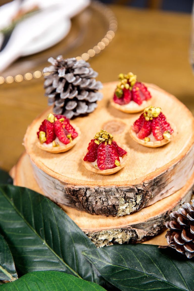 Strawberry tarts with gold flakes atop festive log platter and leaves and pinecones decorations | PartySlate