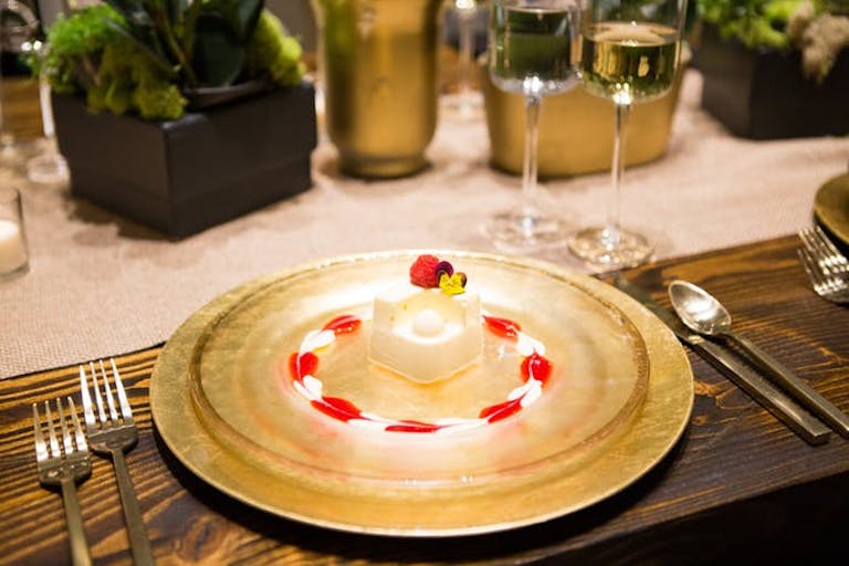 Wooden dinner table with festive panna cotta dessert atop a gold plate and candy cane colored decoration | PartySlate