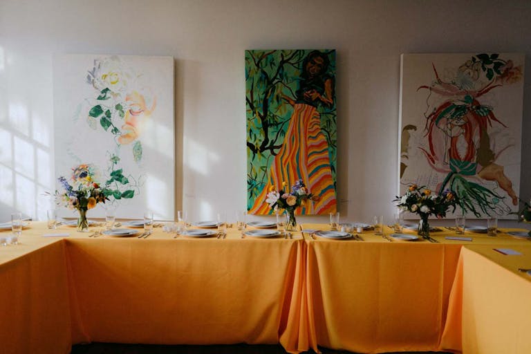 table with orange table cloth and three colorful paintings