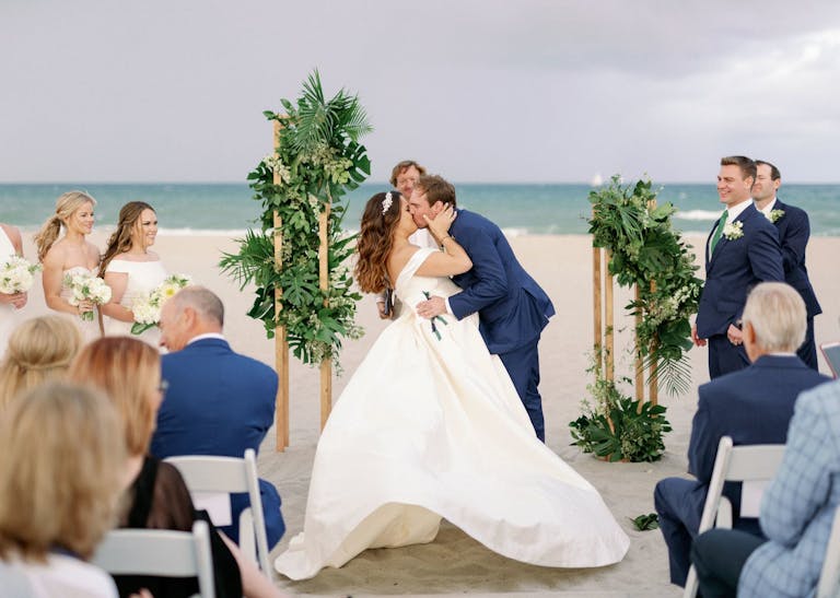 bride and groom kissing at beach ceremony
