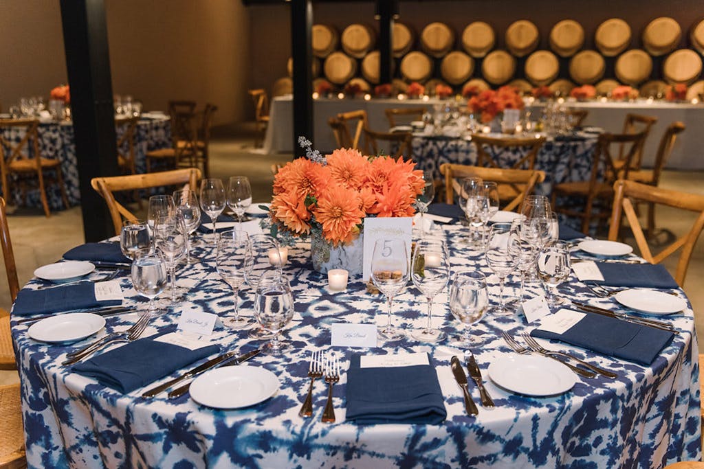 Blue-and-white table cloth with orange floral centerpiece at a wedding rehearsal dinner | PartySlate