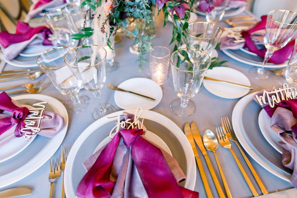 Magenta dinner napkins with each guest's name spelled out in gold lettering at a wedding rehearsal dinner | PartySlate
