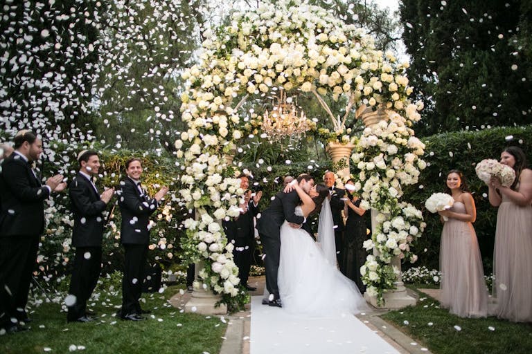 bride and groom kiss during petal toss upon leaving ceremony