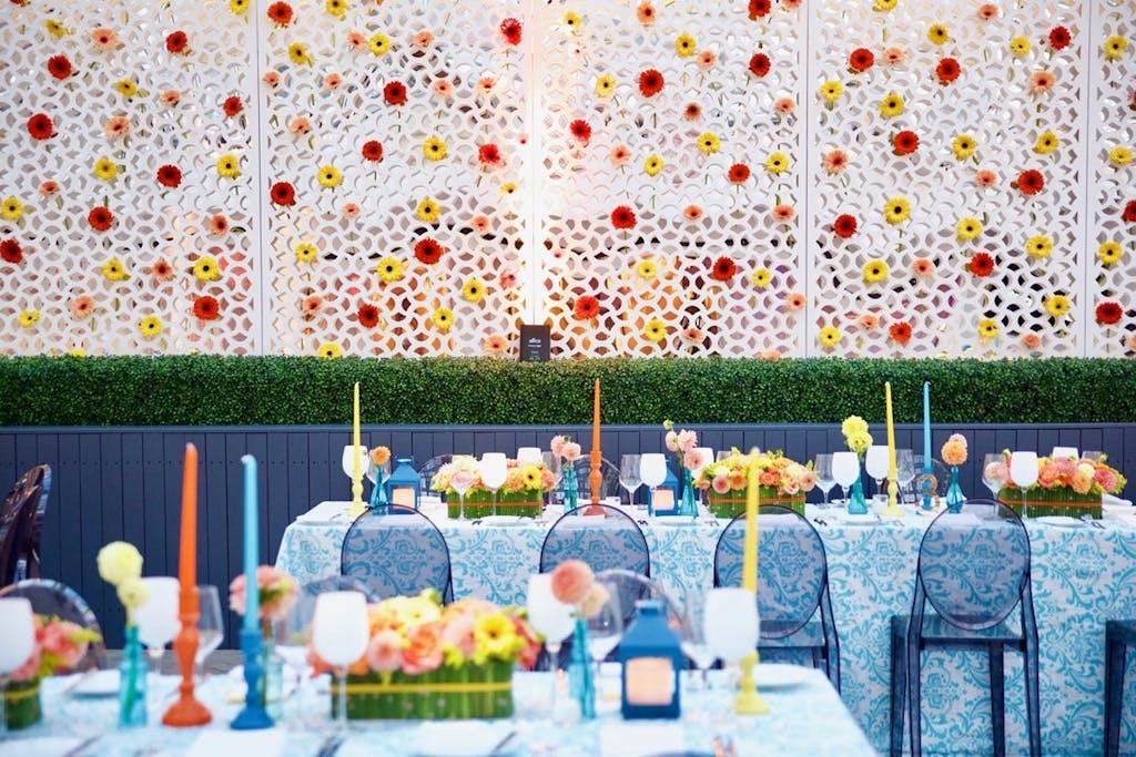La Sirena dining room with colorful tapered candles and a white wall decorated with red and yellow flowers at a wedding rehearsal dinner party | PartySlate