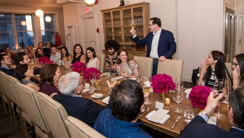 Man raises toast to banquet table full of guests at a wedding rehearsal dinner | PartySlate