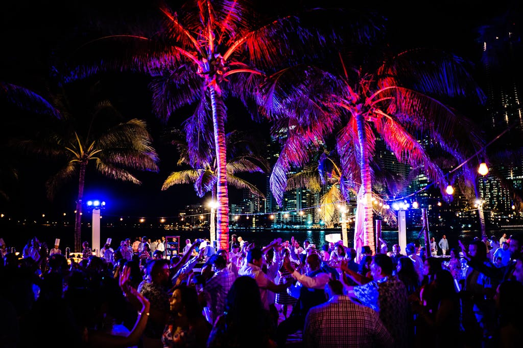 Outdoor wedding rehearsal dinner with colorful uplighting in palm trees
