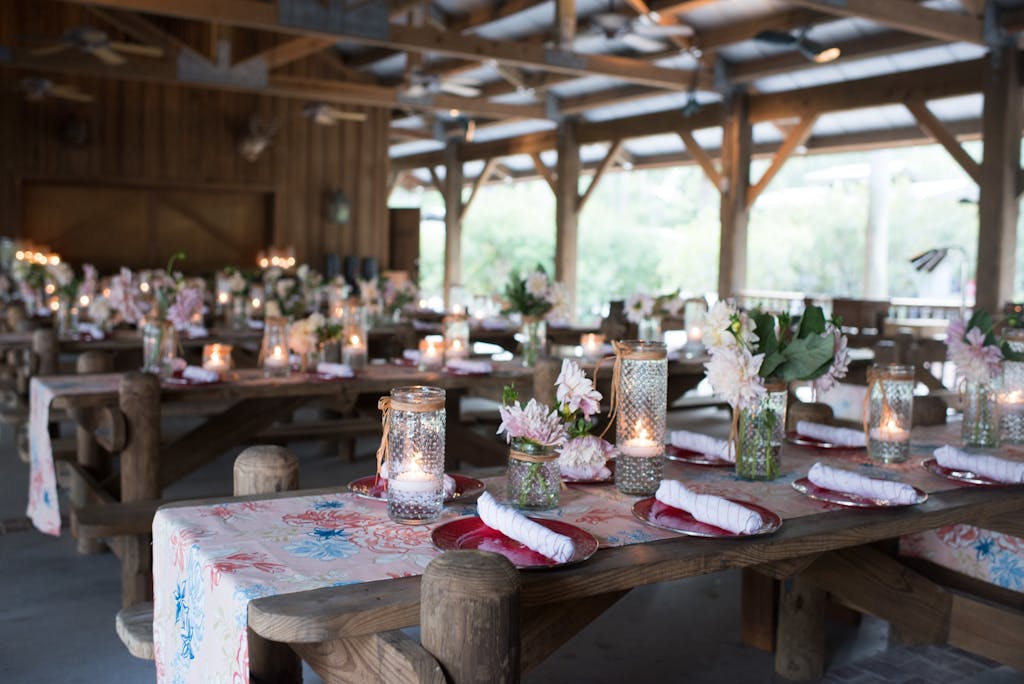 Outdoor rustic space featuring wooden banquet tables with colorful linens at a wedding rehearsal dinner | PartySlate