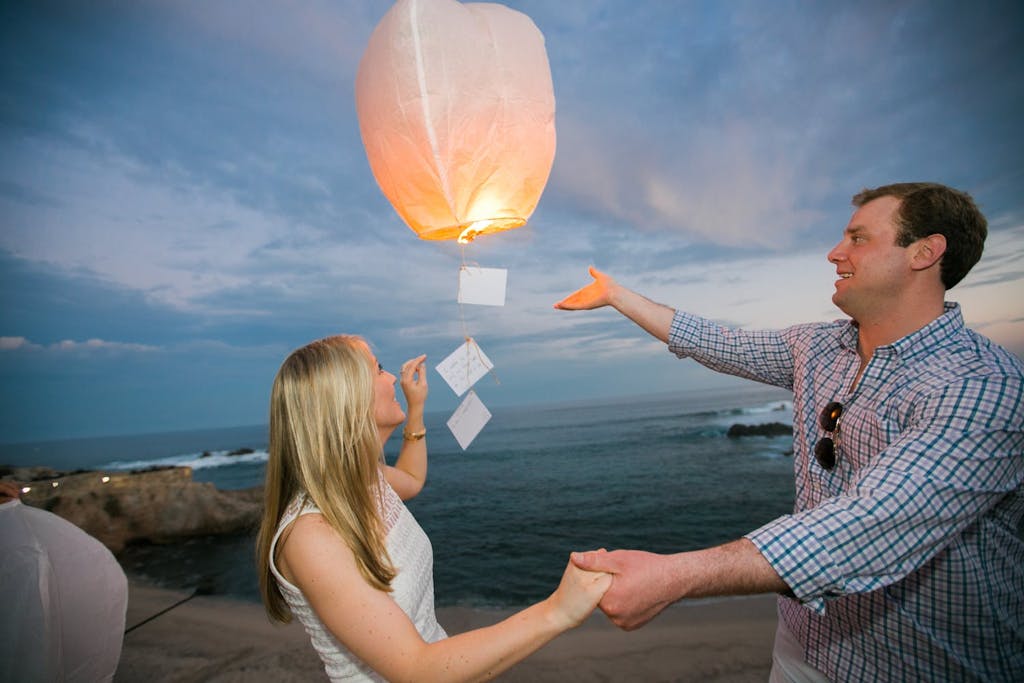 Man and woman releasing wish lantern over ocean at a wedding rehearsal dinner | PartySlate