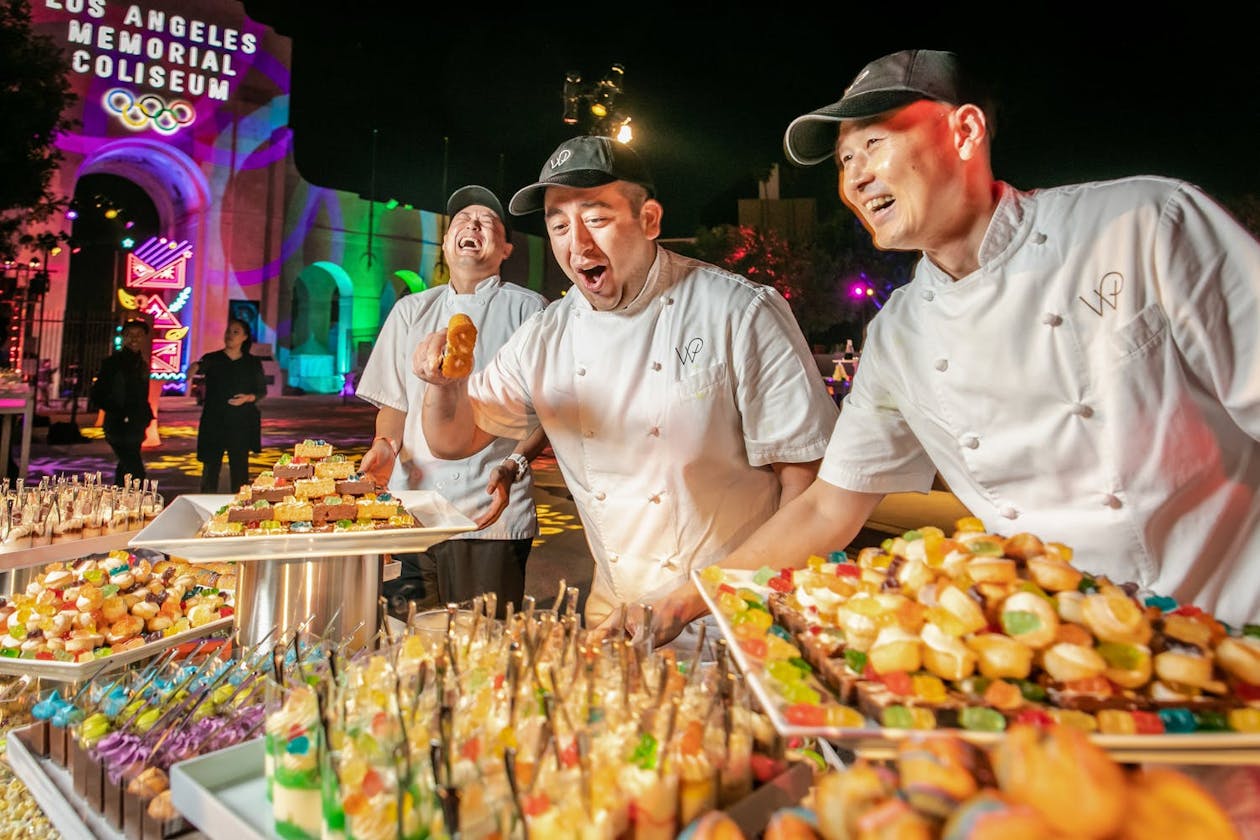 Three caterers laugh happily at their food station.