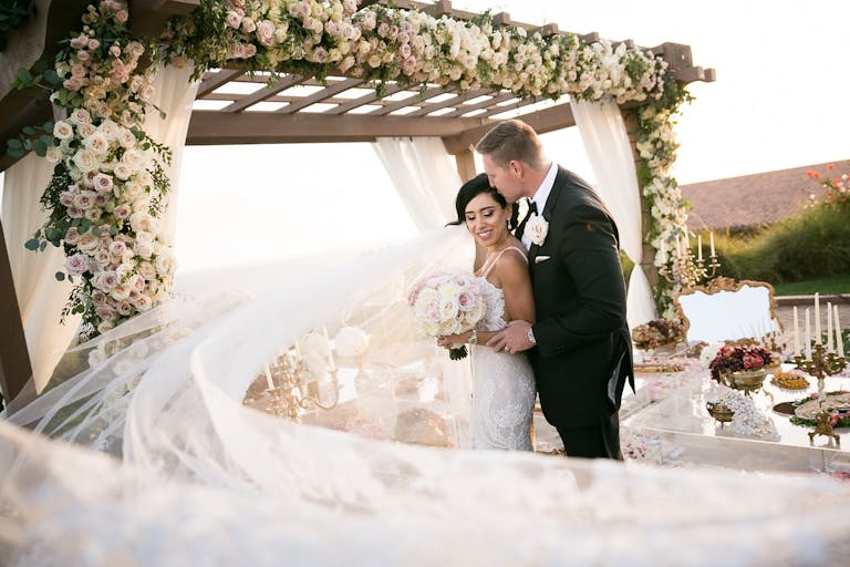 bride and groom in front of flower-decked chuppah with wind-blown veil