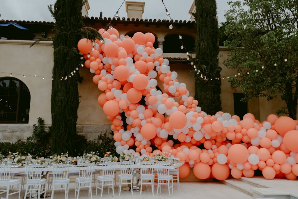 Cascading coral balloon installation in courtyard at a wedding rehearsal dinner party | PartySlate