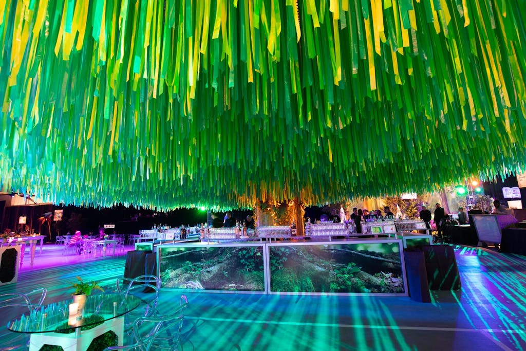 Dense green ribbon hangs from the ceiling over a colorfully lit floor and a mirrored bar. 