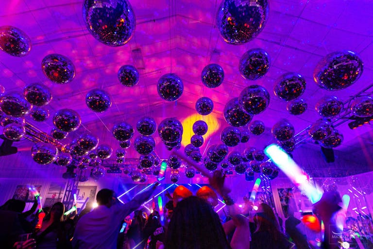 Disco ball covered ceiling above party goers with glow sticks at starlight-inspired Bat Mitzvah | PartySlate