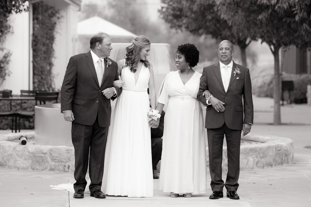 2 brides stand in the middle of each of their fathers, preparing to walk down the aisle.