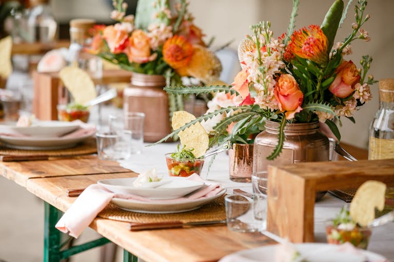 banquet table with coral-colored blooms and salsa cups | PartySlate