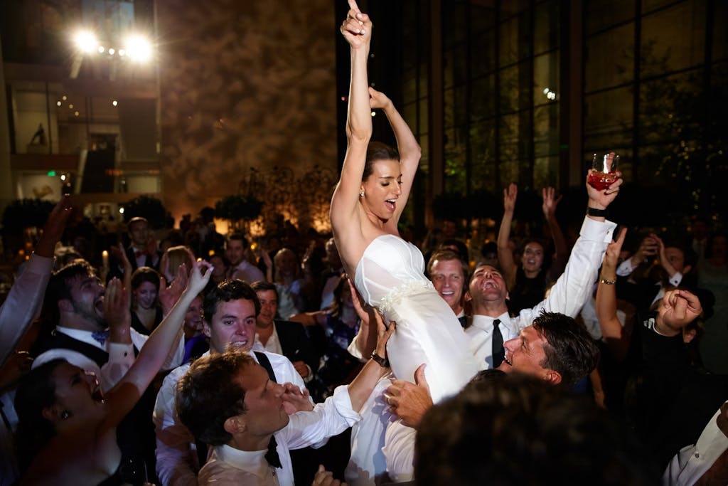 A bride is being lifted by the groomsmen, she has her hands in the air and the crows is laughing and smiling.
