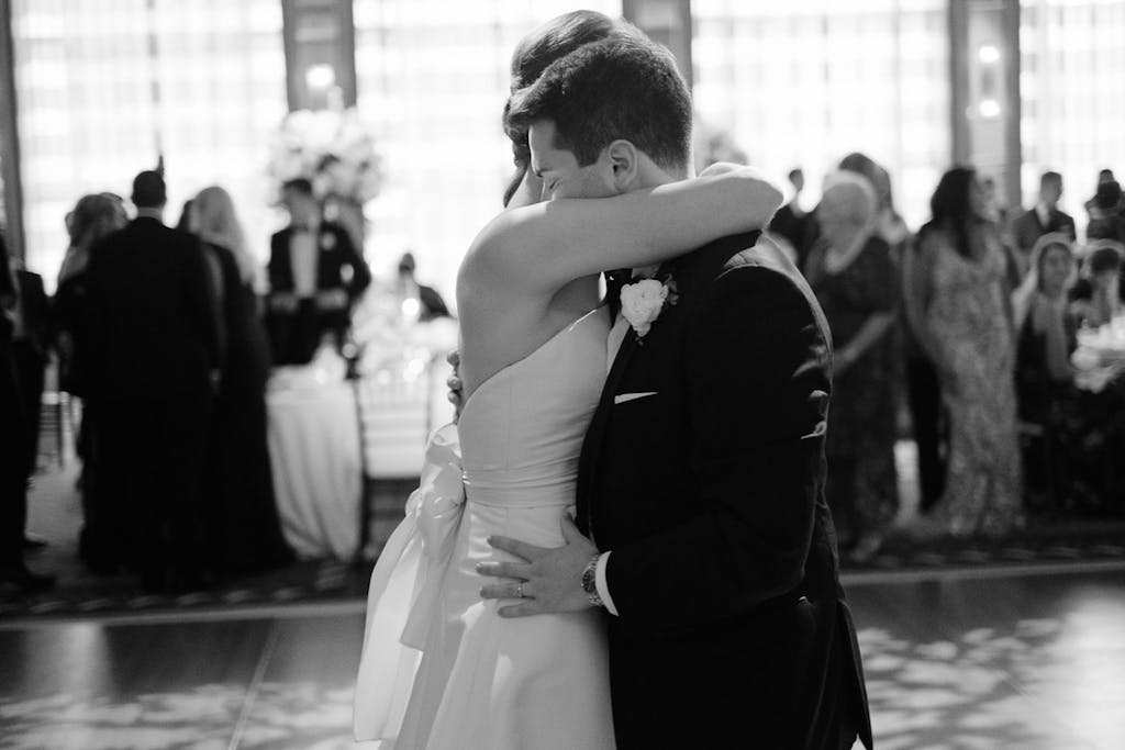 A bride and groom hug on the dance floor. Wedding guests surrounding them.
