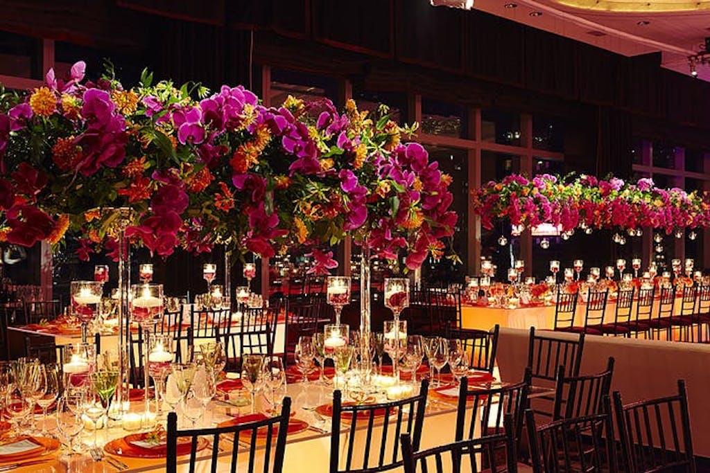 red orchids and bright orange flowers hover over lit tabletops at wedding
