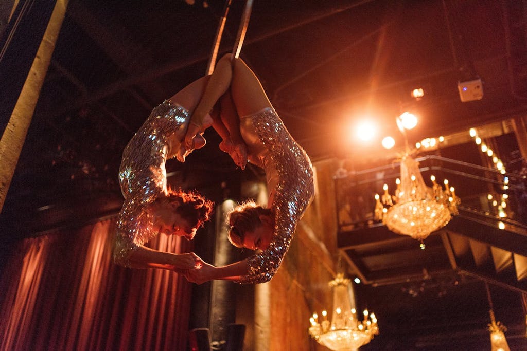 Two aerialists in sequin leotards hand suspended in the air while holding hands