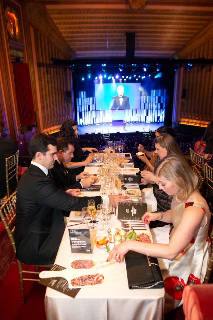 Guests enjoy sit-down dinner with stage and giant screen in background.