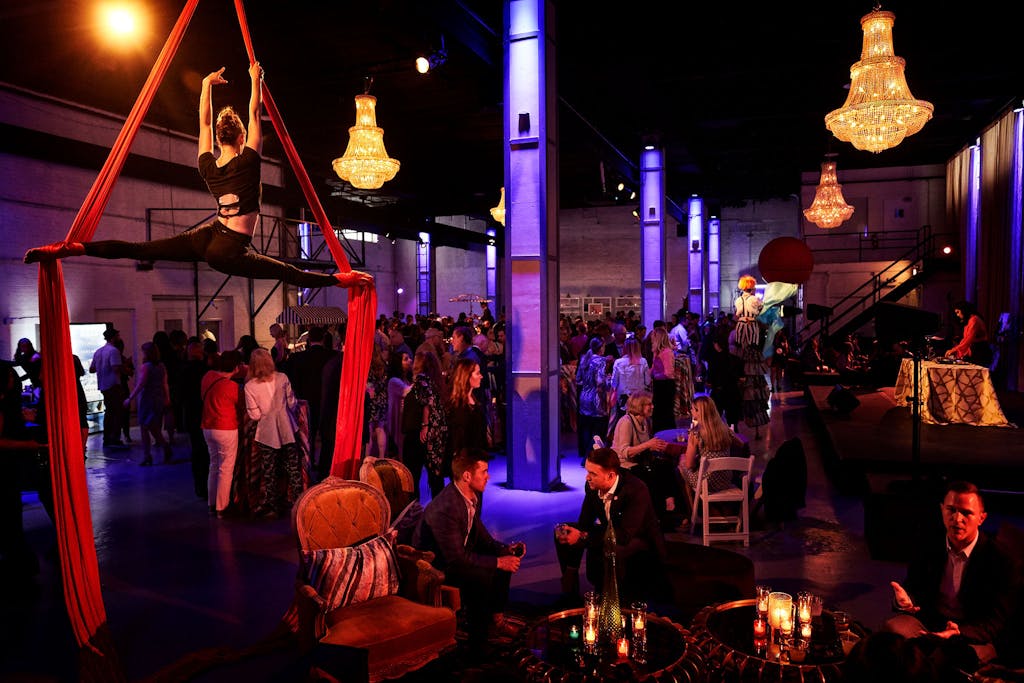 Ballroom with glittery chandeliers, purple up-lit pillars, and aerialist dancers.