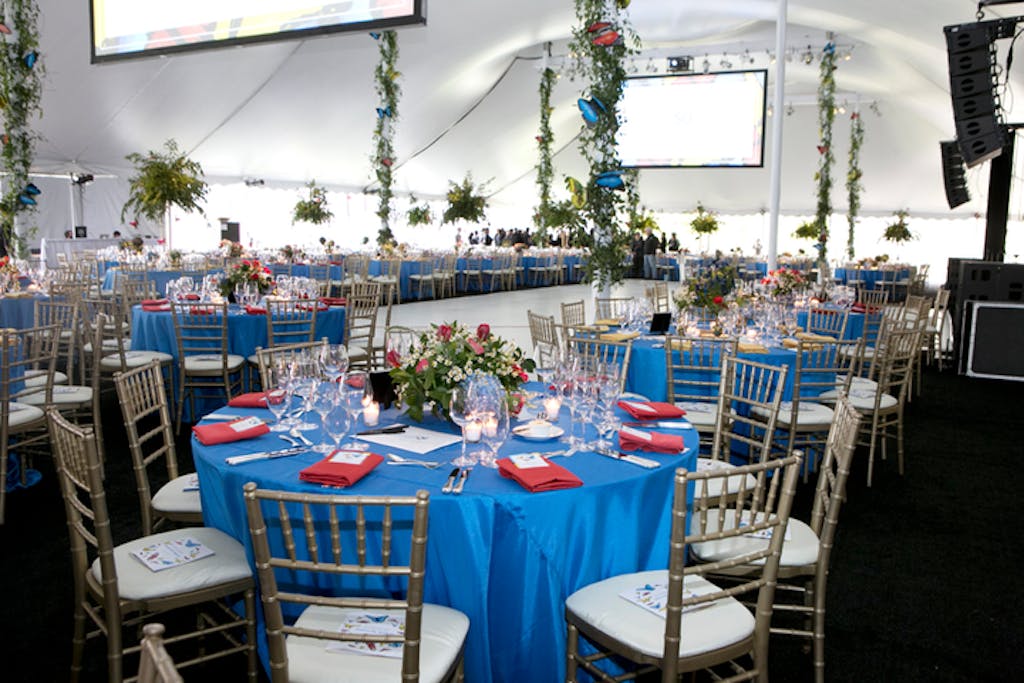 Tented reception room with banquet tables covered in blue linens and red napkins.