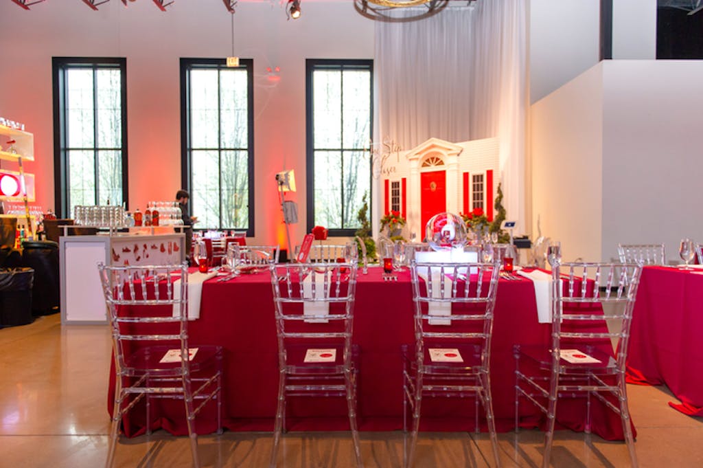 Banquet room featuring table covered in red linens with lucite Chiavari chairs.