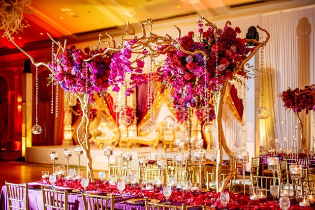 A gold and yellow background and a pink floral centerpice that extends very tall with gold antler-like accents and gold stems. Gold beads hand from the arrangements