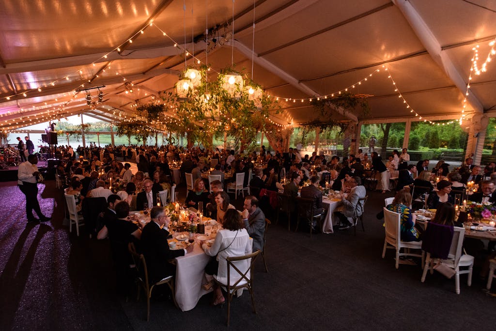 Tented ballroom with string lighting and guests sitting at banquet tables.