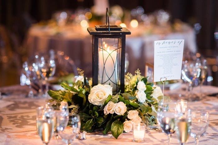 a single candle inside a black lantern with small leafy greens and white florals surrounding