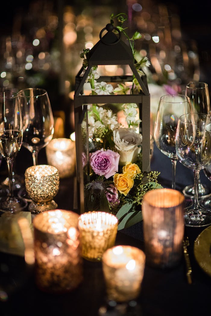 several gold flaked votive candles surrounding a lantern with purple and yellow florals inside
