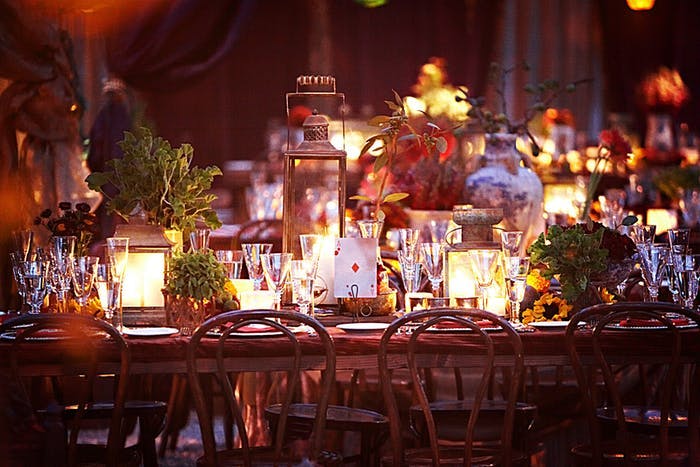 Glowing votive candles make the photo glow yellow and gold. Cone shaped wine glasses are placed at each setting and a tall copper lantern is in the center.