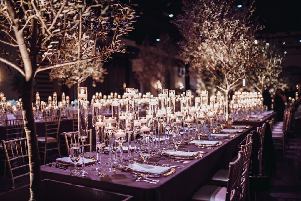 Banquet hall with two candlelit rectangular tables and winter tree foliage.