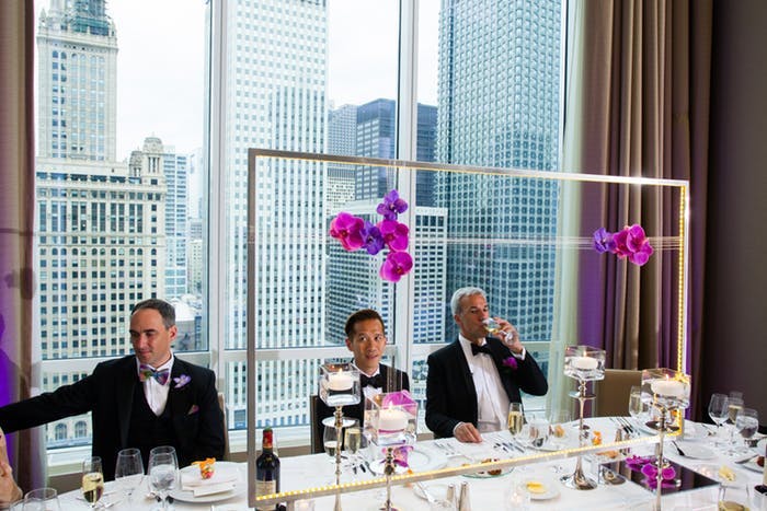 Simple pink and purple orchids hang from a geometric structure on a wedding reception table.