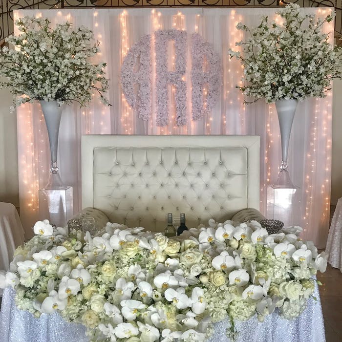 A sweetheart table with a cushioned background with green and white orchid wedding centerpieces