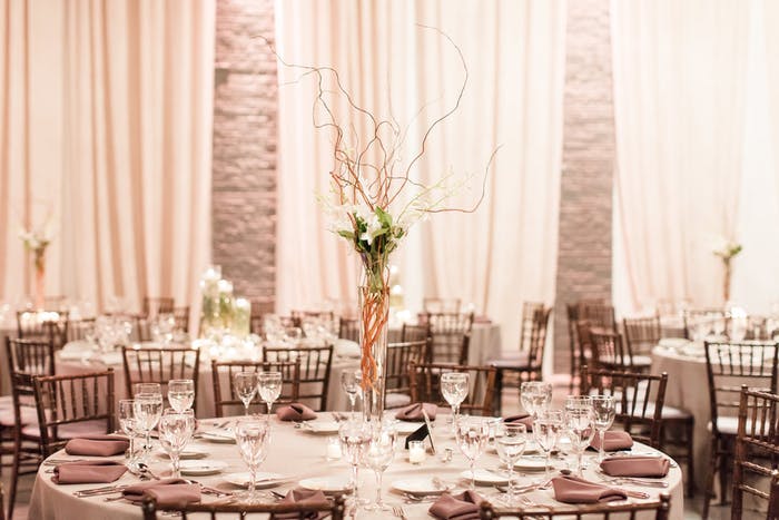 A monochromatic grey room with drapery in the background. The middle ground showcases a twiggy and branchy centerpiece that is tall with white floral accents