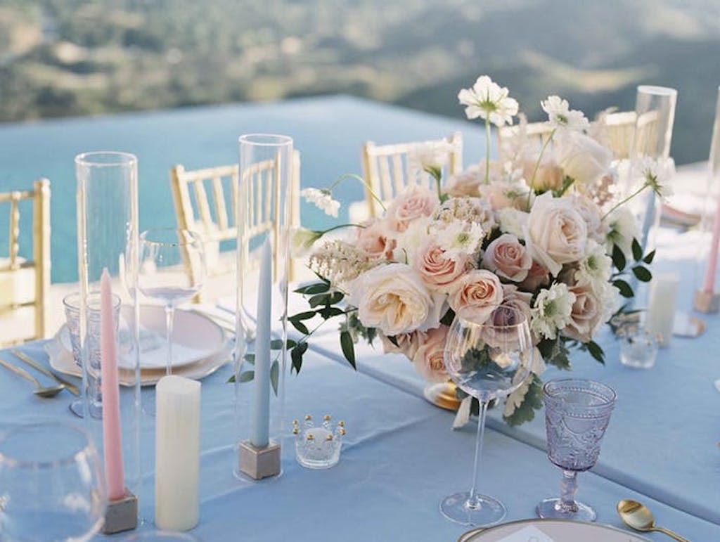 Pink and blue pillar candles juxtaposed with pale pink floral arrangements over looking the pool.