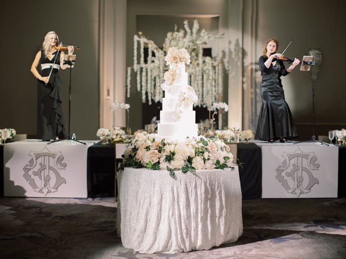 multi-tiered white wedding cake on a center table with musicians on the stage behind it