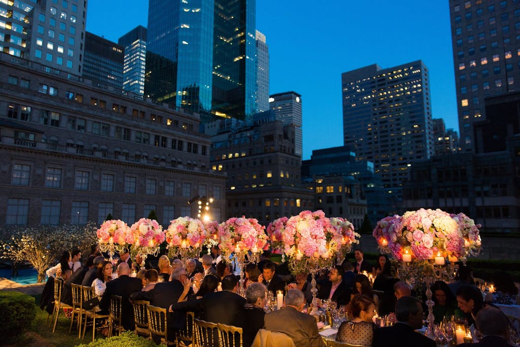 Banquet table with lit up pink floral arrangements at outdoor evening reception in New York City.