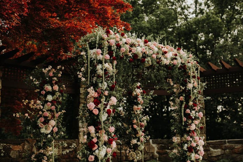 An archway covered in pale pink and white florals mixed with draping greenery 