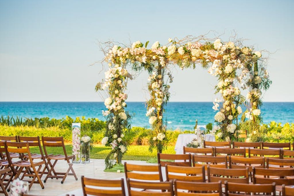 Two archways covered in green and white florals in front of bright blue water.