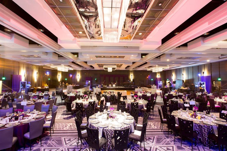 A ballroom with round tables and a pink ceiling.
