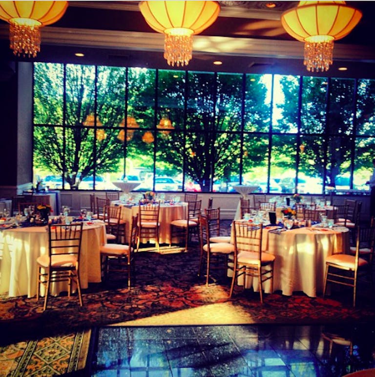 Concorde Banquets baby shower venue in Chicago with tables with white linens and wooden chairs. Large paned windows look out to greenery and trees